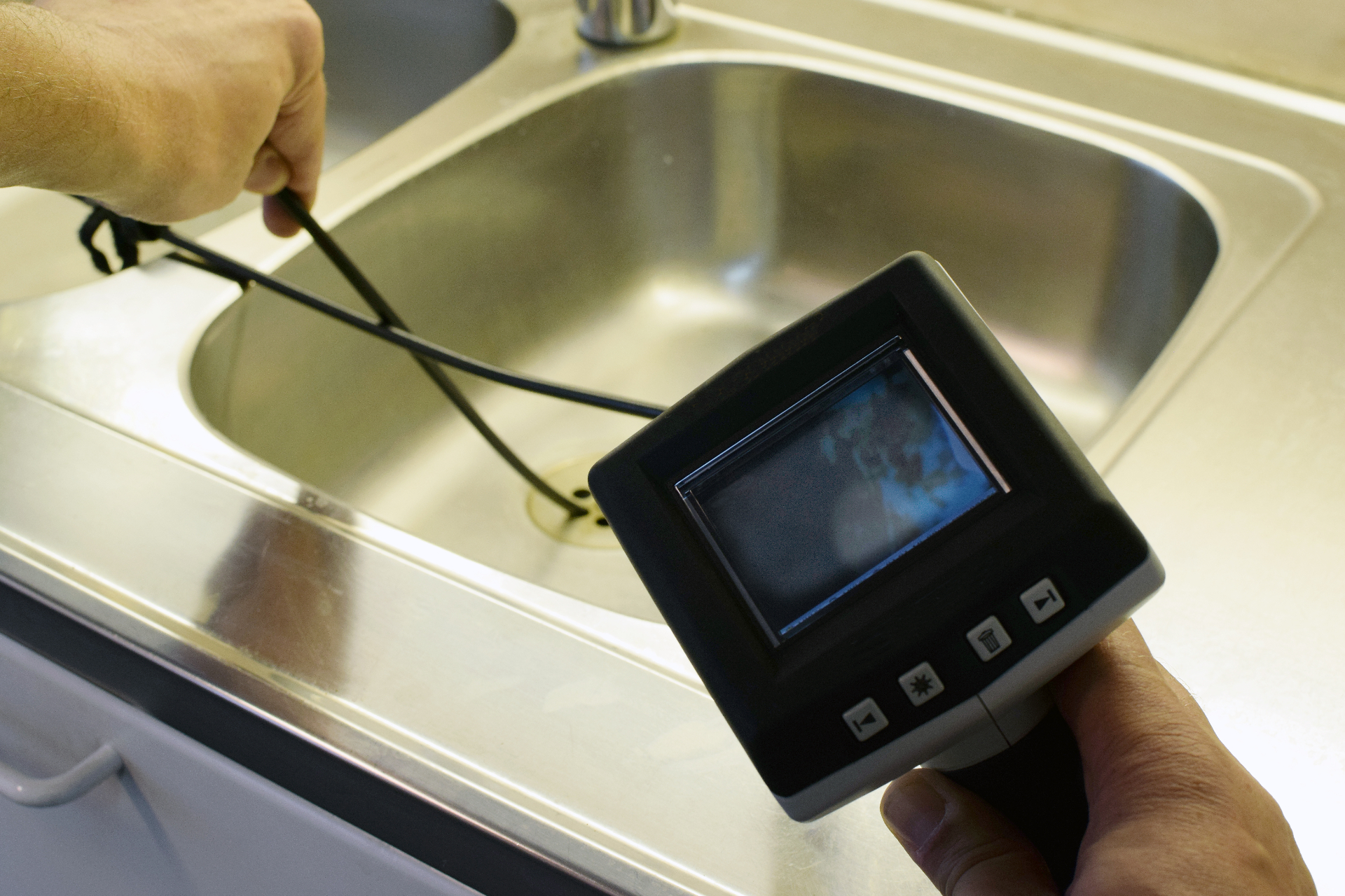 Plumber using a sewer inspection camera monitor at a kitchen sink
